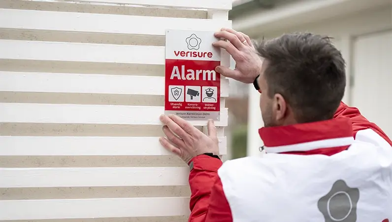 Mann fester alarmskilt fra Verisure på en vegg